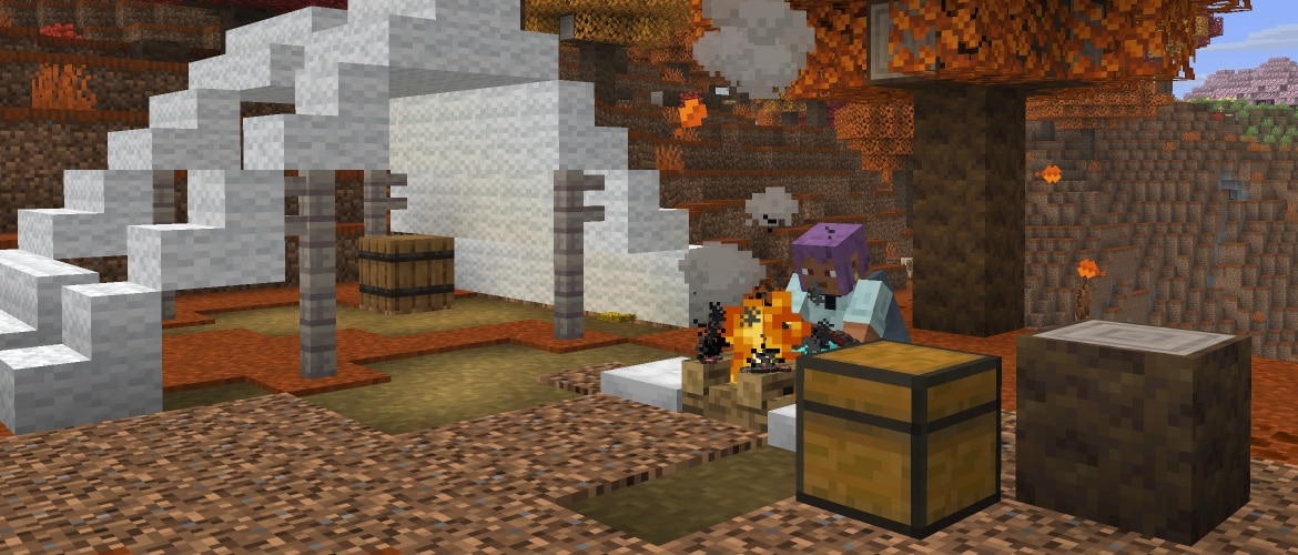Efe is sitting on a cushion in front of a camp fire in an abandoned camp in a dappled forest.