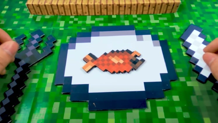 Image of a pixelated orange and yellow fish sitting atop a pixelated white and black plate, inspired by Minecraft