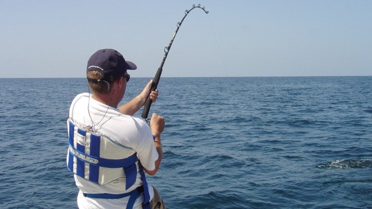 A man seen from the back, fishing in the ocean.