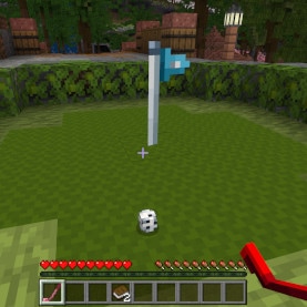 Minecraft gameplay scene with a white flagpole planted on a grassy arena. A small golf ball sits on the ground while the player holds a red golf club in hand
