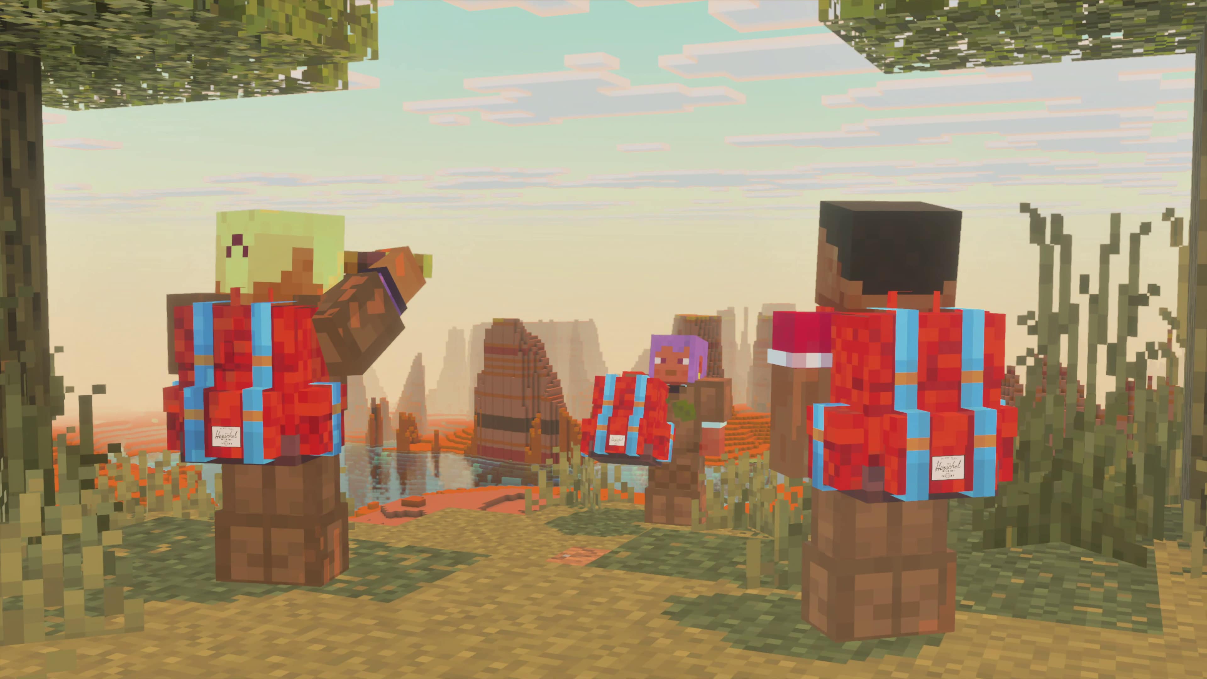 Three players wearing red Herschel backpacks overlook a scenic badlands landscape from a grassy hilltop at sunrise.