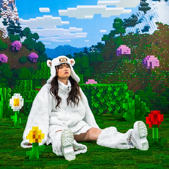 A photo of a model wearing the Sheep sherpa and ushanka from the Minecraft x Cool Shirtz collection, inside an Overworld setting
