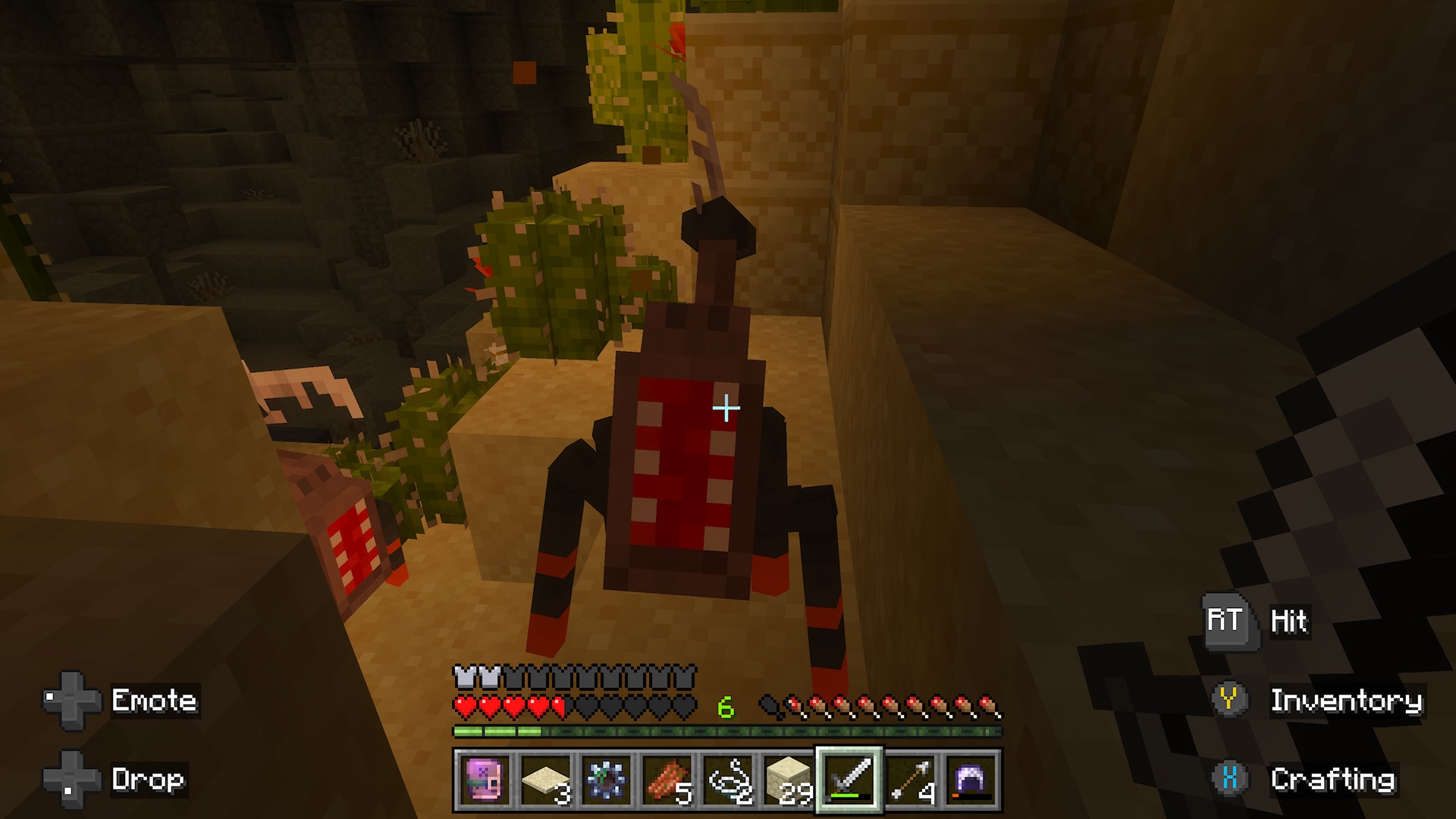 Minecraft player confronts a large red-and-black insect-like creature among cacti and sandy blocks in an underground cave.