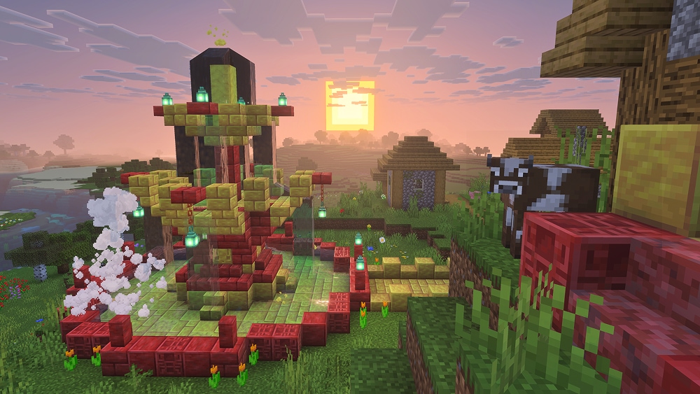 A tall red and yellow fountain with hanging green lanterns stands beside a Minecraft village at sunset, with steam rising from the left side.