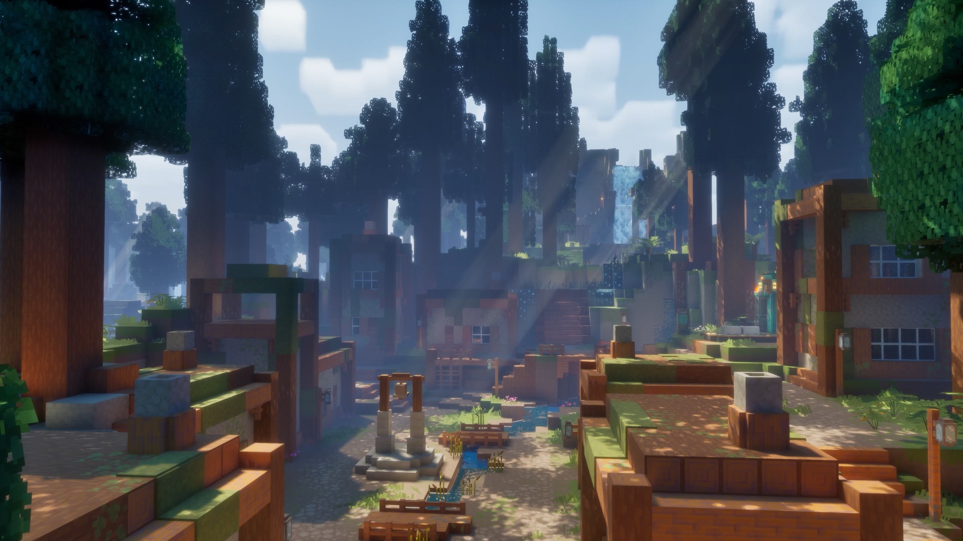 A wide view of a forest village with blocky houses, stone paths, wooden bridges, and tall trees, with sunlight streaming through the canopy in the background.